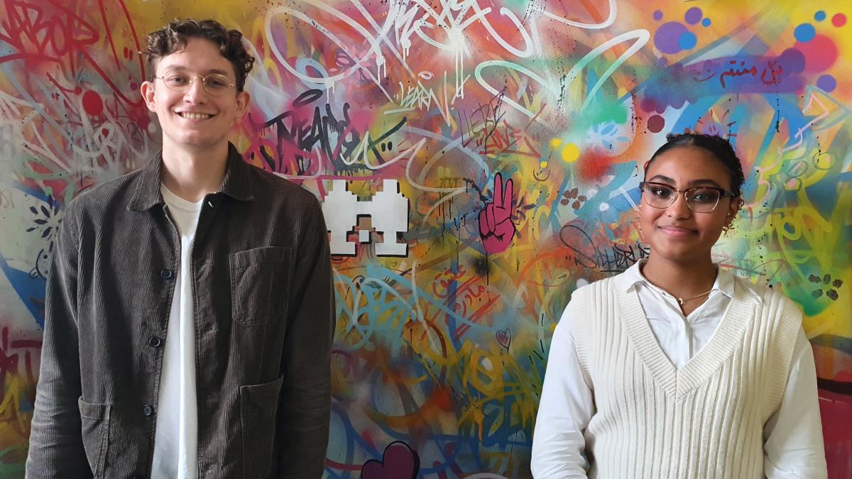 Zwei Auszubildende des BAMF stehen vor einer bunten Wand und lächeln. (Quelle: BAMF) Zwei Auszubildende des BAMF stehen vor einer bunten Wand und lächeln.