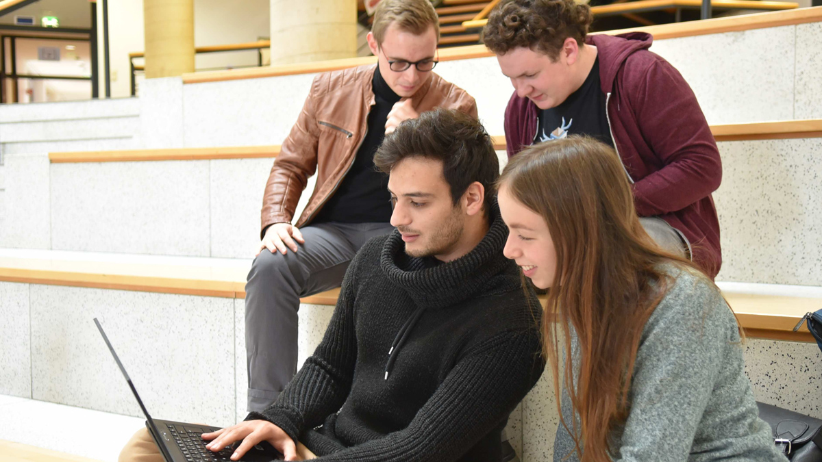 Vier junge Menschen sitzen auf Treppenstufen und schauen auf den Bildschirm eines Laptops. (Quelle: HS Bund) Vier junge Menschen sitzen auf Treppenstufen und schauen auf den Bildschirm eines Laptops.